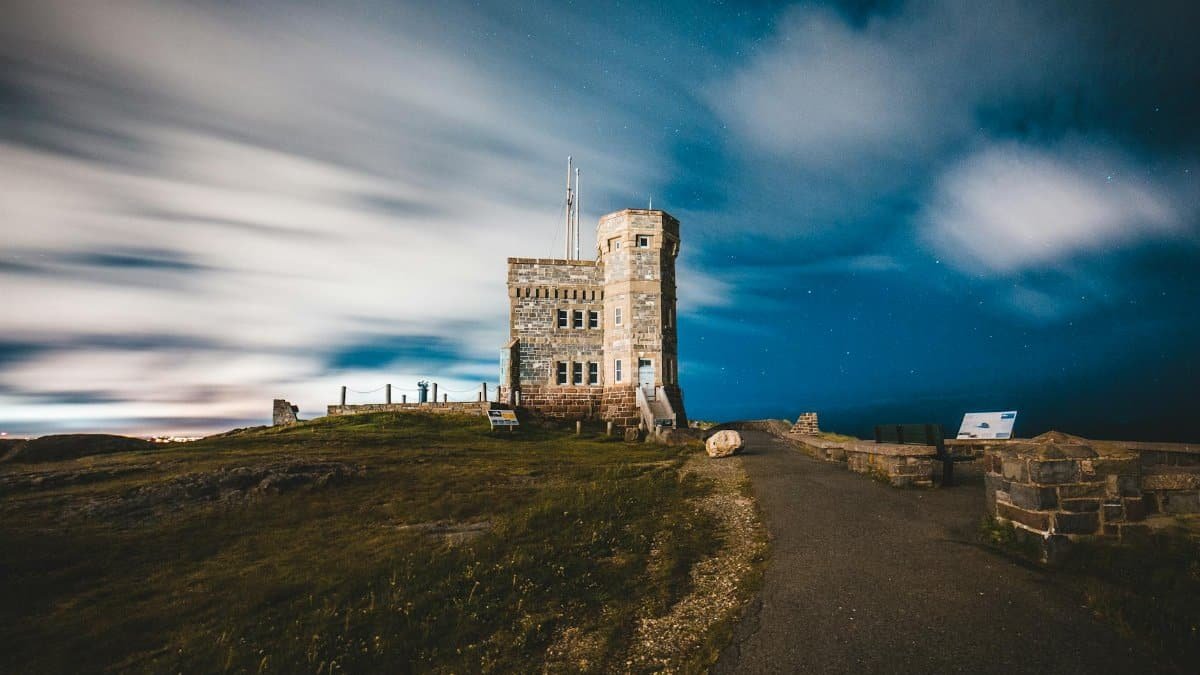 A picturesque stone tower stands by the sea under a starry night sky with dramatic clouds.