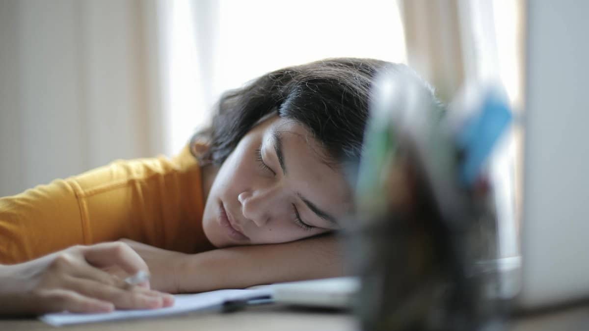 Young woman in yellow shirt resting her head on a desk, showing signs of fatigue and relaxation indoors.