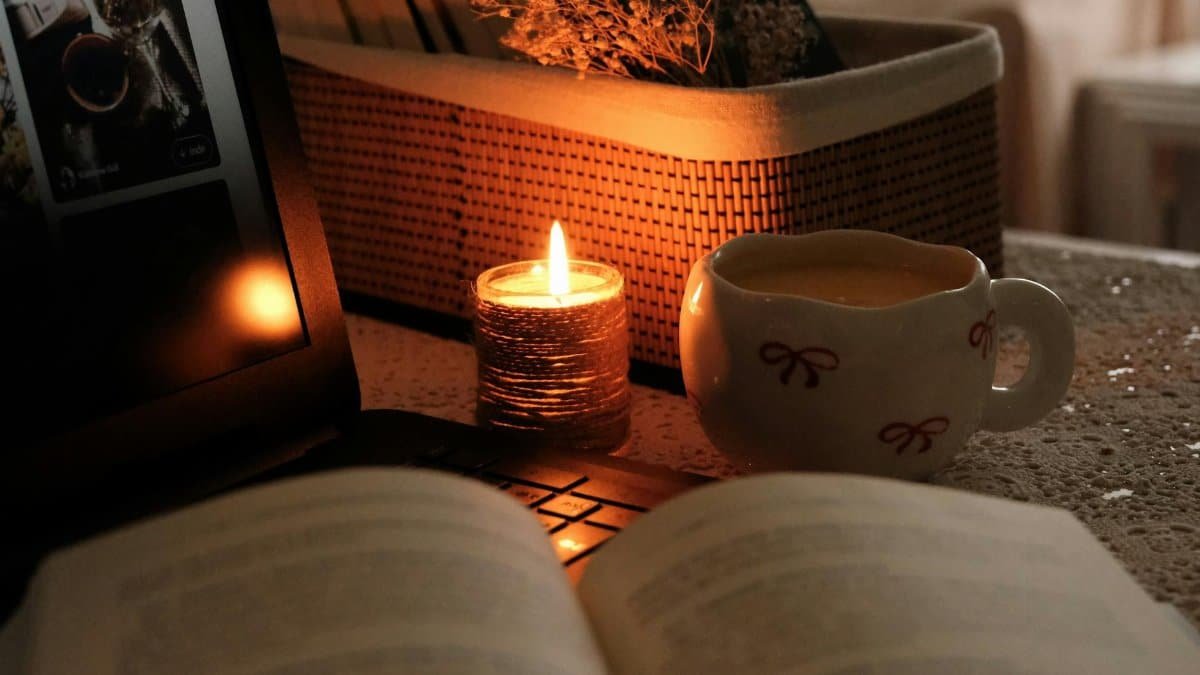 Warm and cozy evening scene with candlelight, a cup of drink, and an open book.
