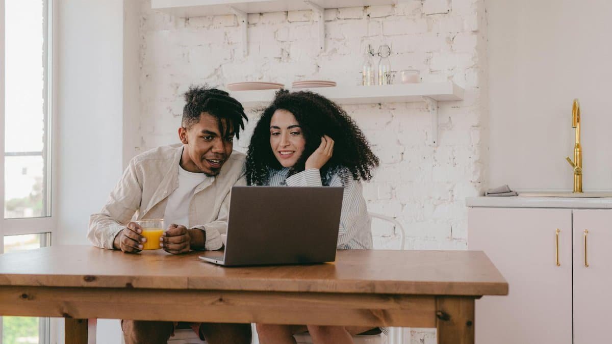 A cheerful couple sitting at a dining table, using a laptop in their cozy home.