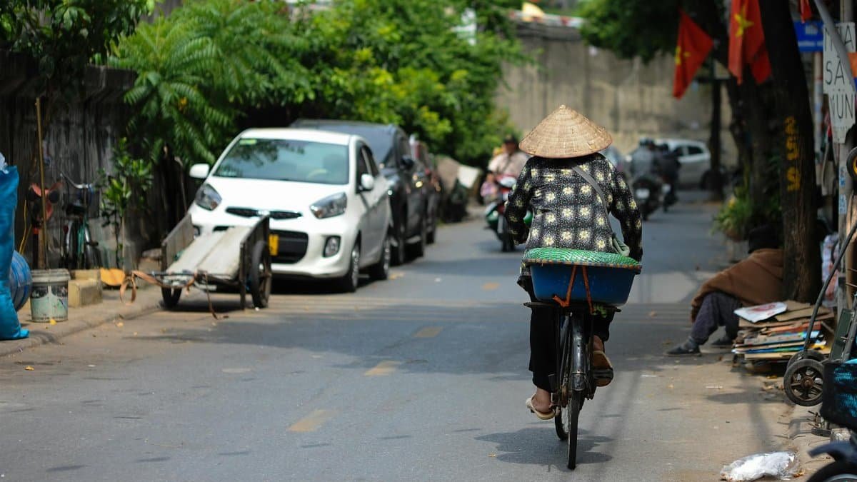Woman on bicycle in Vietnamese street with conical hat, vibrant urban life.
