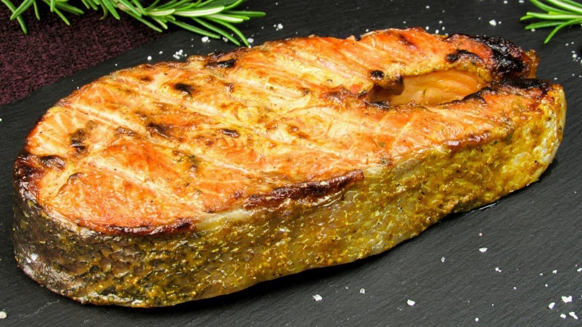 Delicious grilled salmon steak garnished with fresh rosemary on a slate board.