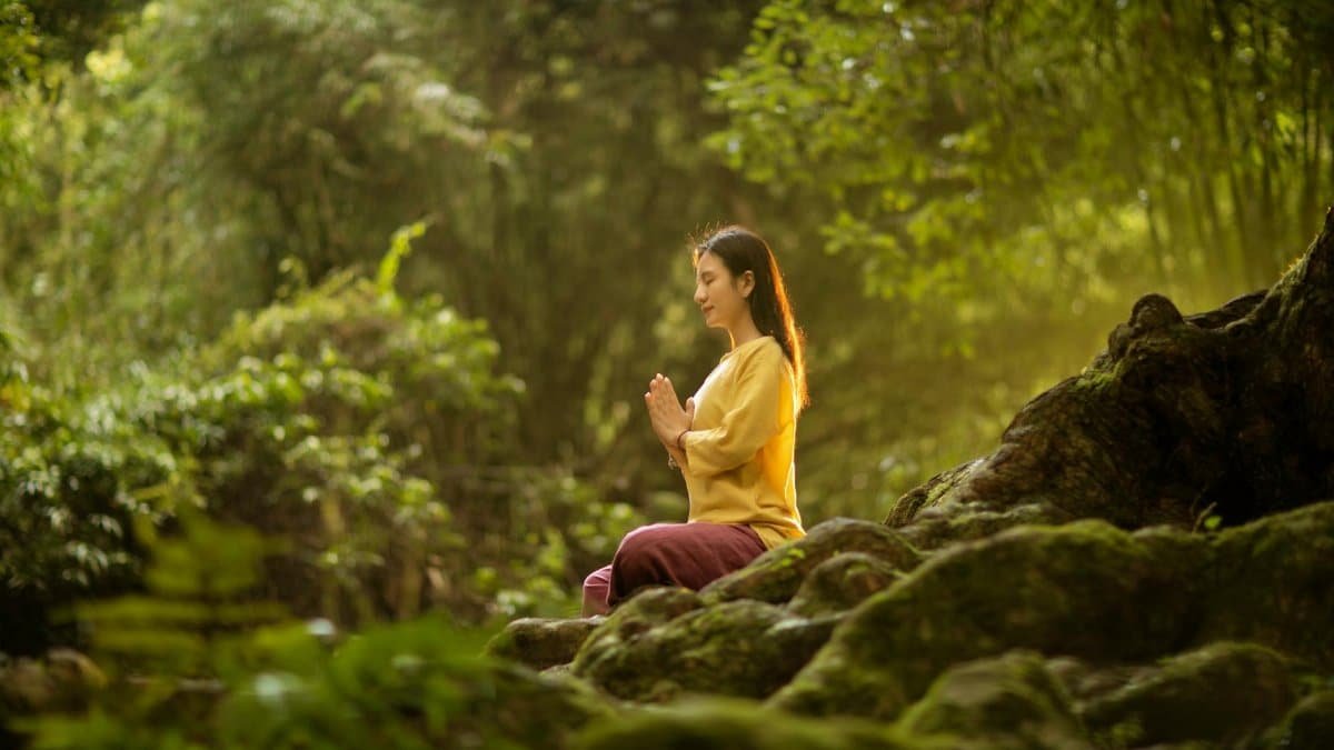 A woman meditates peacefully in a sunlit forest, embodying tranquility and connection with nature.