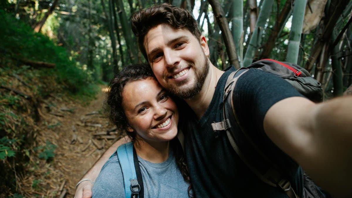 A joyful couple taking a selfie during a hike through a lush forest trail.