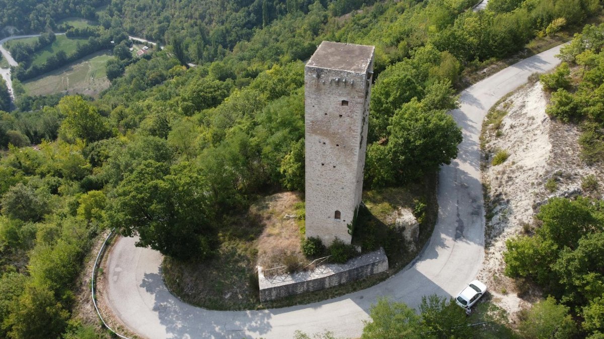 Drone view of ancient tall stone tower surrounded by rural road loop and located on verdant forested hill slope on sunny summer day