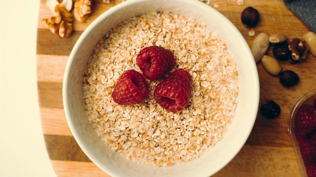 Top view of a white bowl with oatmeal, raspberries, and nuts on a wooden board, perfect for a healthy breakfast.