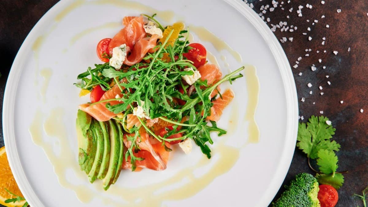 A top-view shot of a vibrant salmon and avocado salad with arugula, cherry tomatoes, and feta cheese.