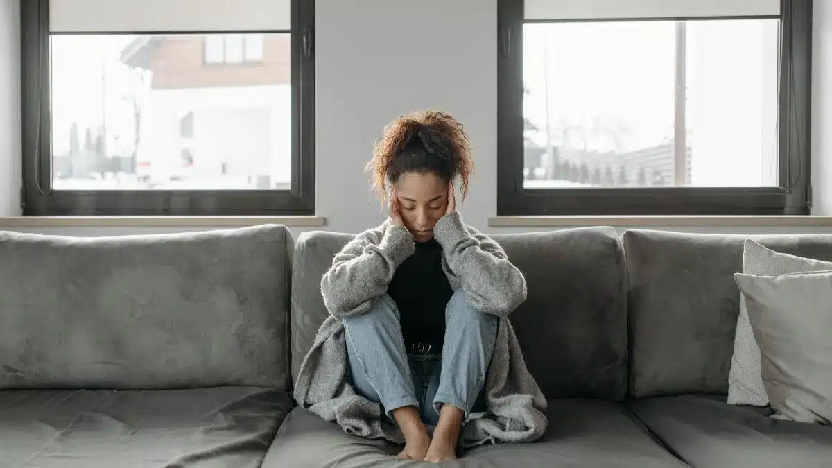 A woman sits on a sofa looking unwell, emphasizing a sense of illness or fatigue indoors.