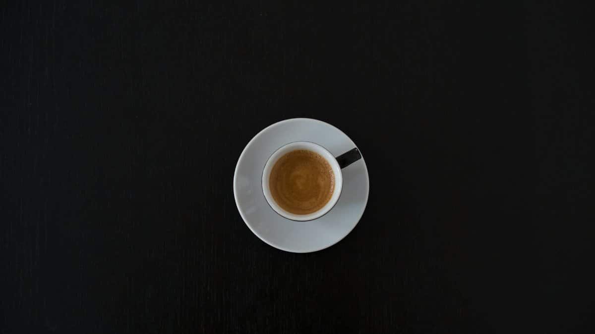 Flat lay of a white coffee cup with espresso on a black table, highlighting minimalist design.