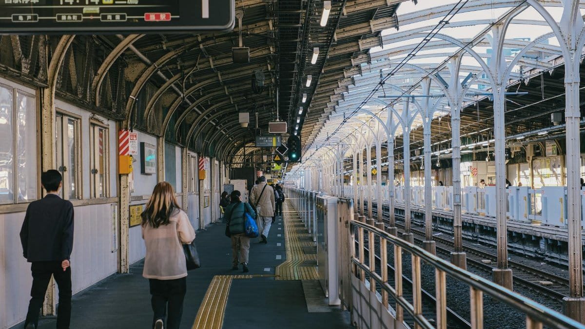 Commuters walking along a bustling train station platform under a covered structure.
