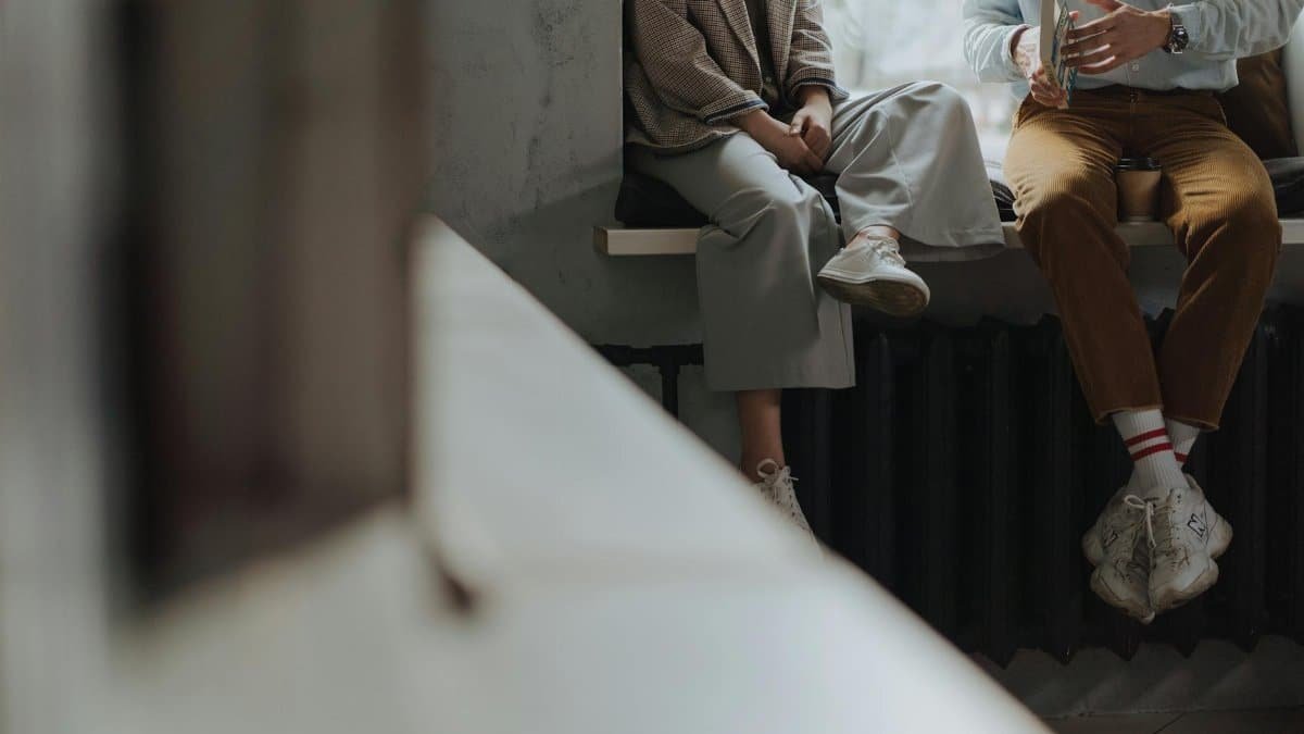 Two adults sitting and chatting by a window, enjoying leisure time indoors.