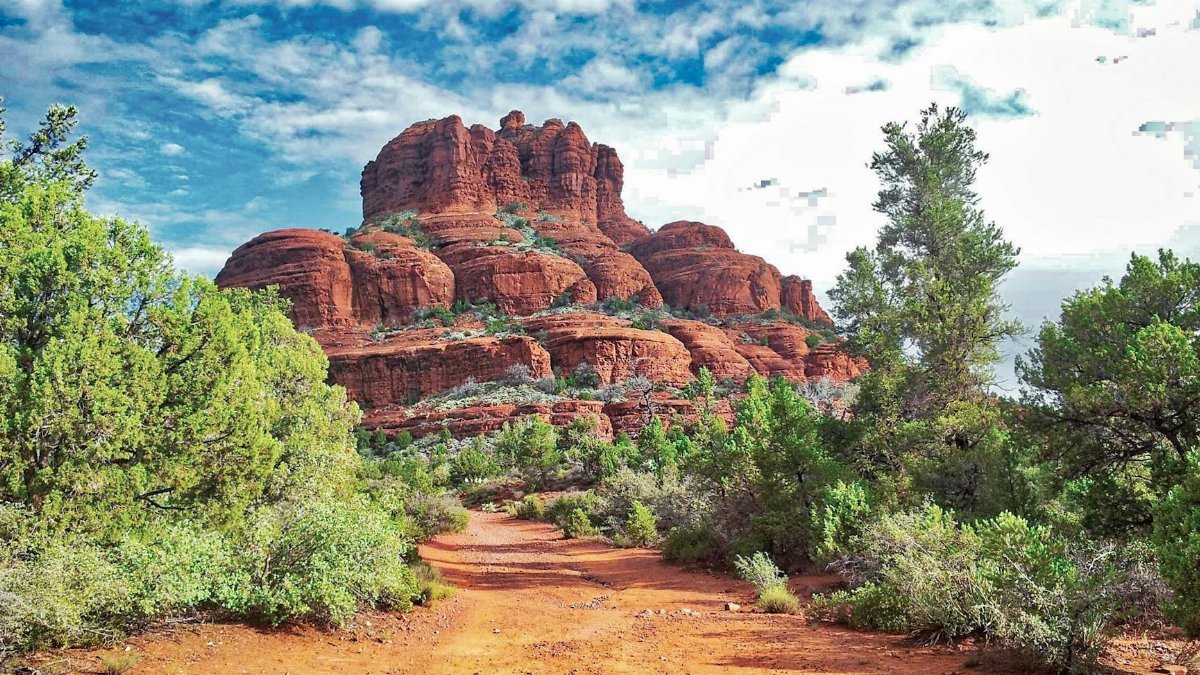 Beautiful red rock formations in Sedona, Arizona, surrounded by lush greenery under a vibrant sky.