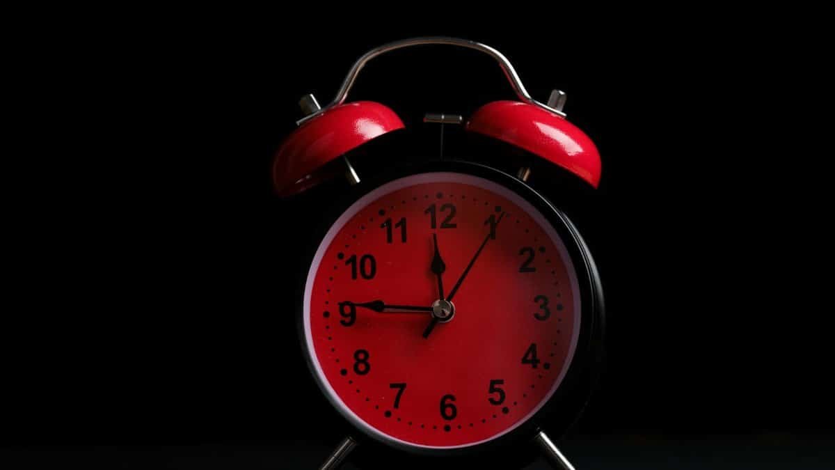 Retro analog alarm clock with red face and bells, showcasing classic design on a black backdrop.