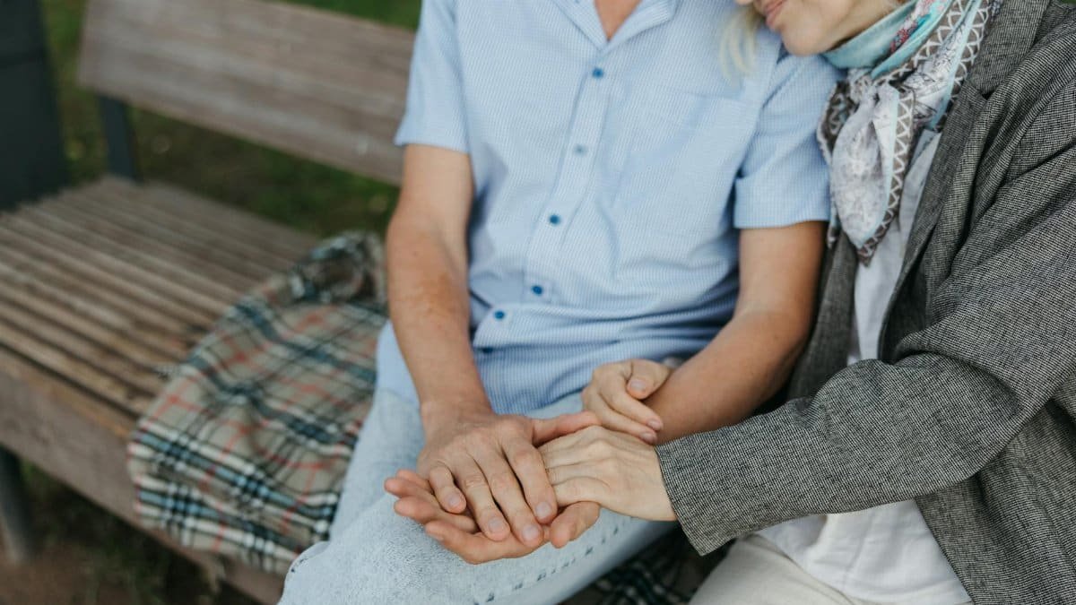 A touching moment of an elderly couple holding hands on a park bench symbolizing love and companionship.