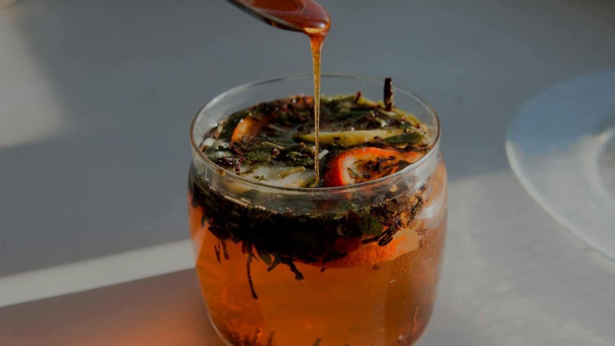 Close-up of a citrus herbal tea with honey being drizzled from a spoon, capturing warm sunlight.
