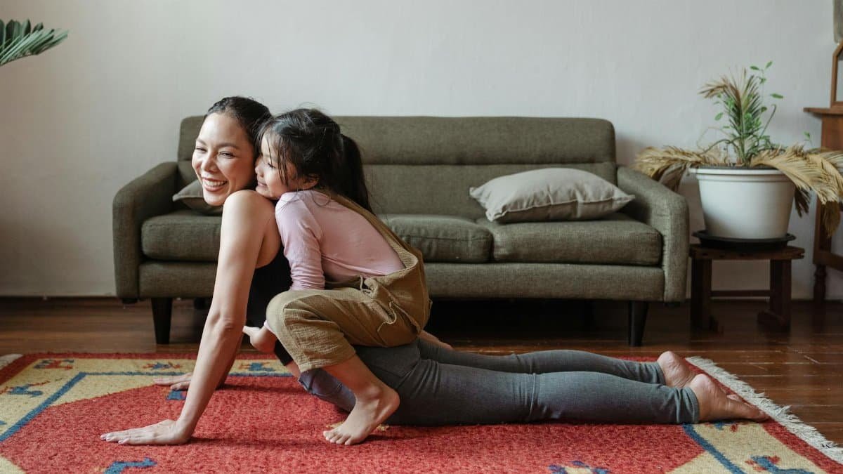 A joyful mother practicing yoga with her daughter on a colorful rug indoors.