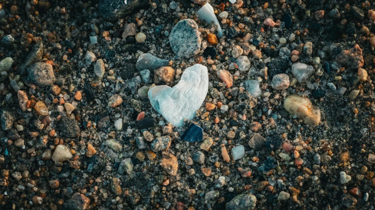 A heart-shaped white stone surrounded by pebbles on a sandy beach.