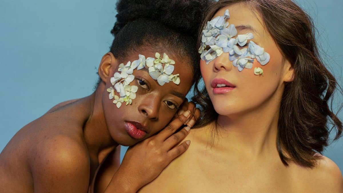 Close-up portrait of two women adorned with delicate flowers, embracing beauty and diversity.