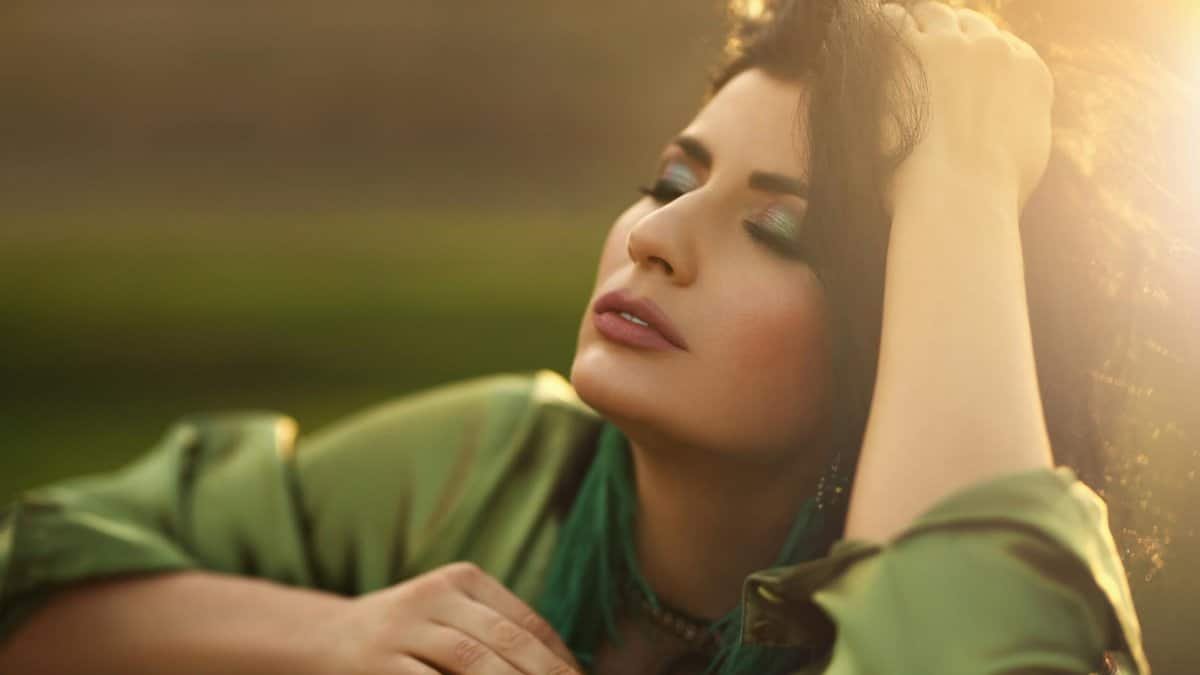 Relaxed female with long messy hair and makeup leaning on wooden barrier in nature