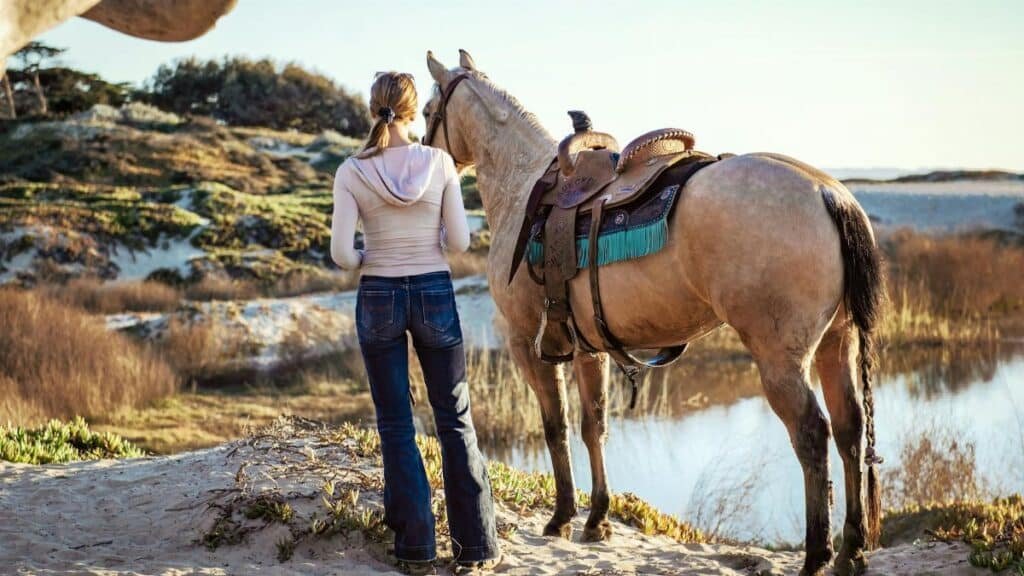 A woman stands with her horse near a body of water at Grover Beach, California, capturing a serene outdoor moment.