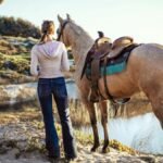 A woman stands with her horse near a body of water at Grover Beach, California, capturing a serene outdoor moment.