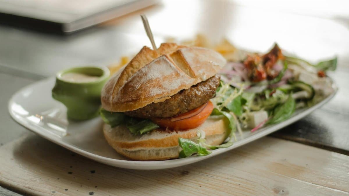 Delicious gourmet burger served with a side of fresh salad and dressing, perfect for a tasty meal.