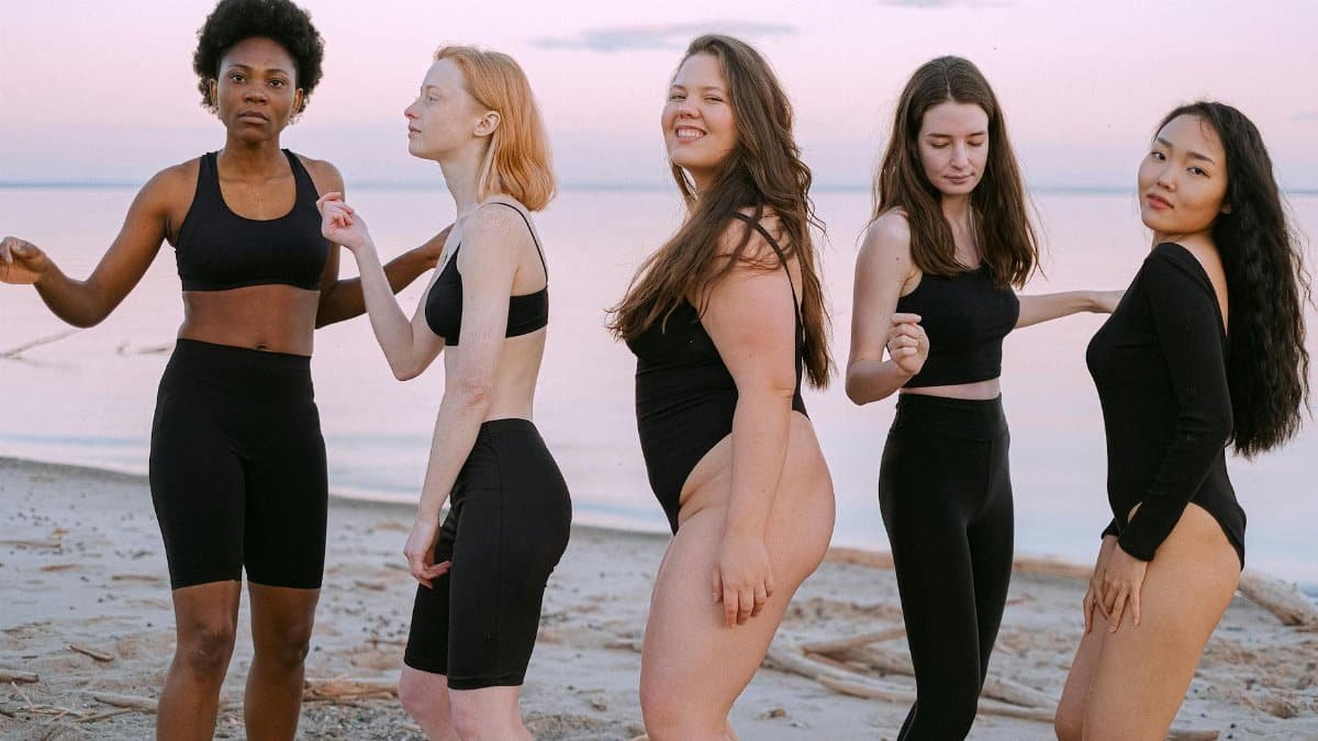 Group of diverse women in activewear enjoying a sunset at the beach, celebrating body positivity and friendship.