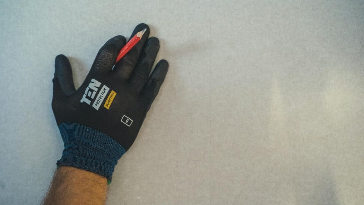 A gloved hand holding a pencil against a textured wall surface, ready for repair work.