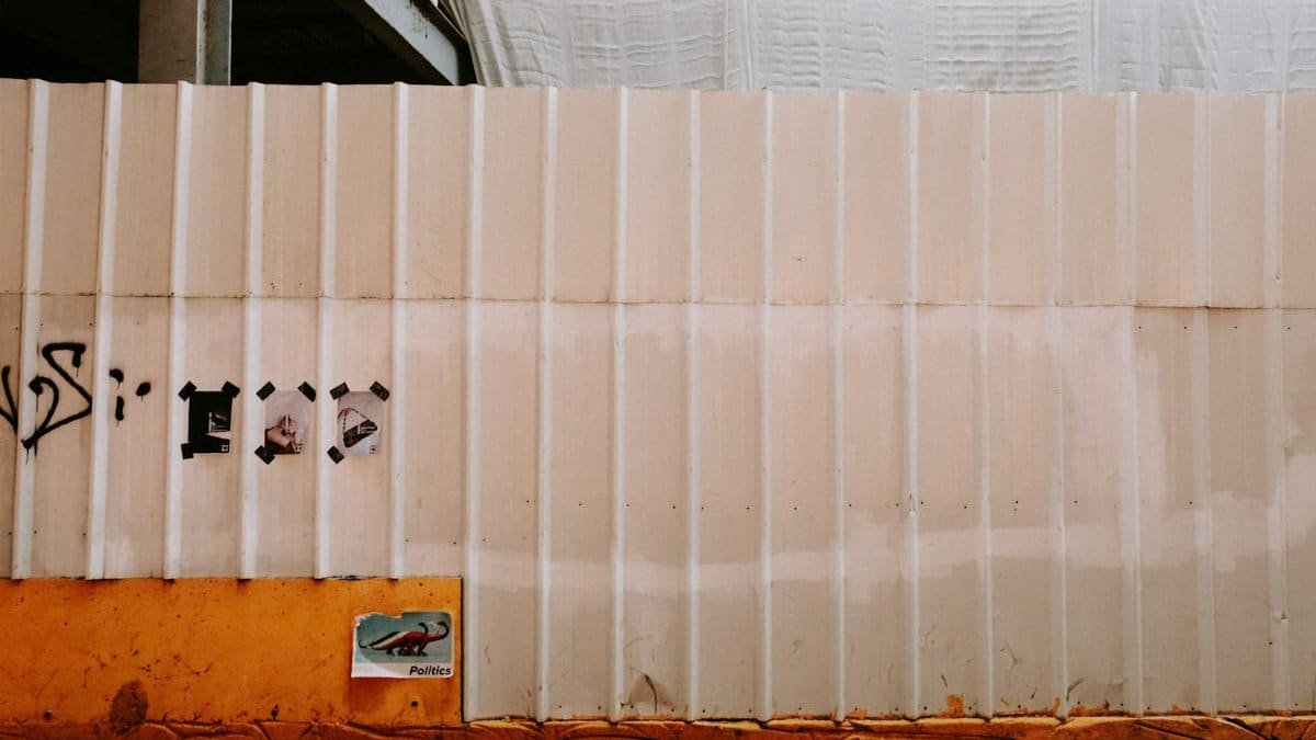 Metal fence in an urban setting with graffiti and a political poster beneath. Captured outdoors.