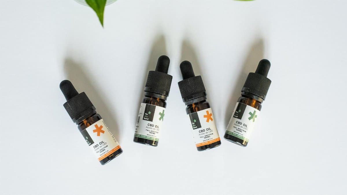 Four CBD oil bottles arranged on a white background with leaves.