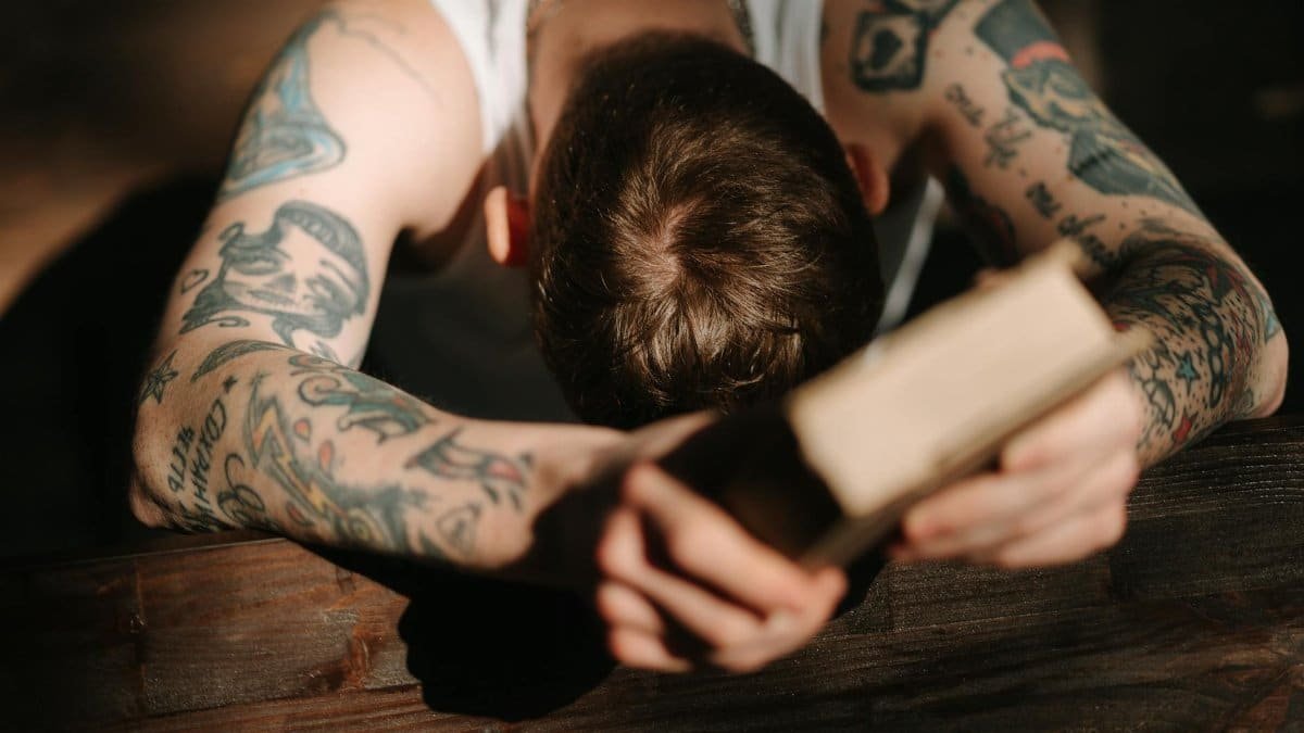 A tattooed man with a bible, deep in prayer, captured from a high angle, conveying faith and repentance.