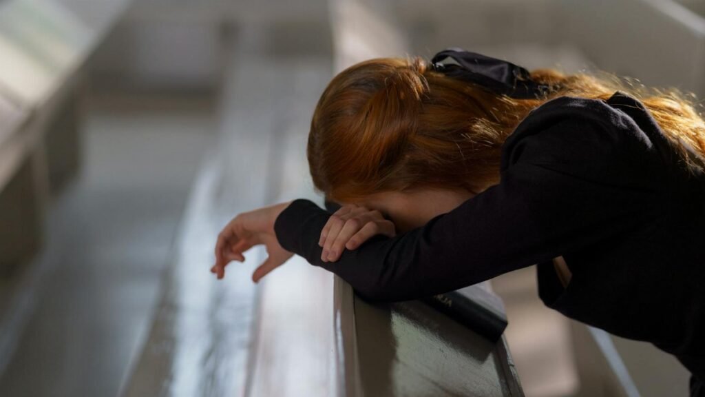 A redheaded woman in deep prayer, leaning on a church pew in a serene atmosphere.