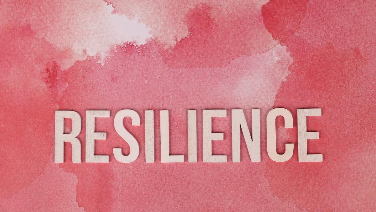 Word 'Resilience' on a pink watercolor background, symbolizing strength.