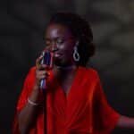 An elegant female singer in a vibrant red dress performs passionately with a vintage microphone.