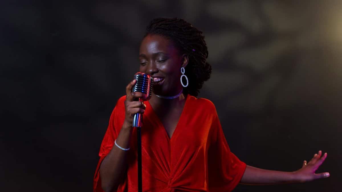 An elegant female singer in a vibrant red dress performs passionately with a vintage microphone.