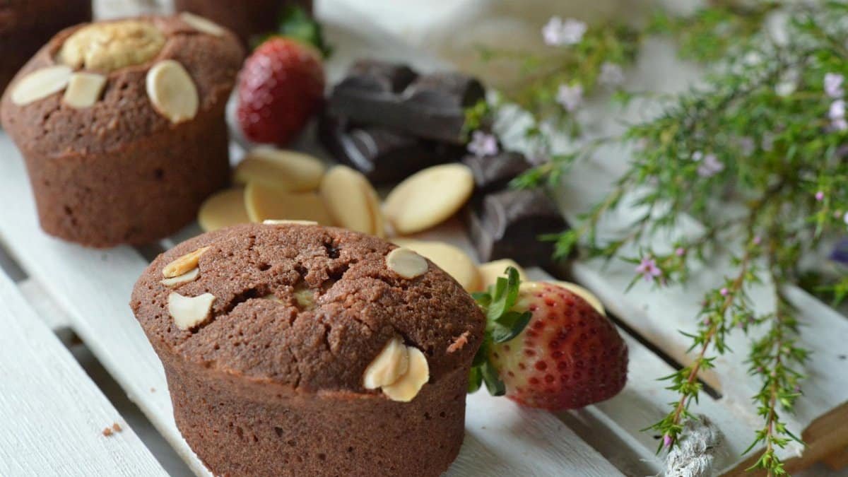 Freshly baked chocolate almond muffins with strawberries on a wooden tray.