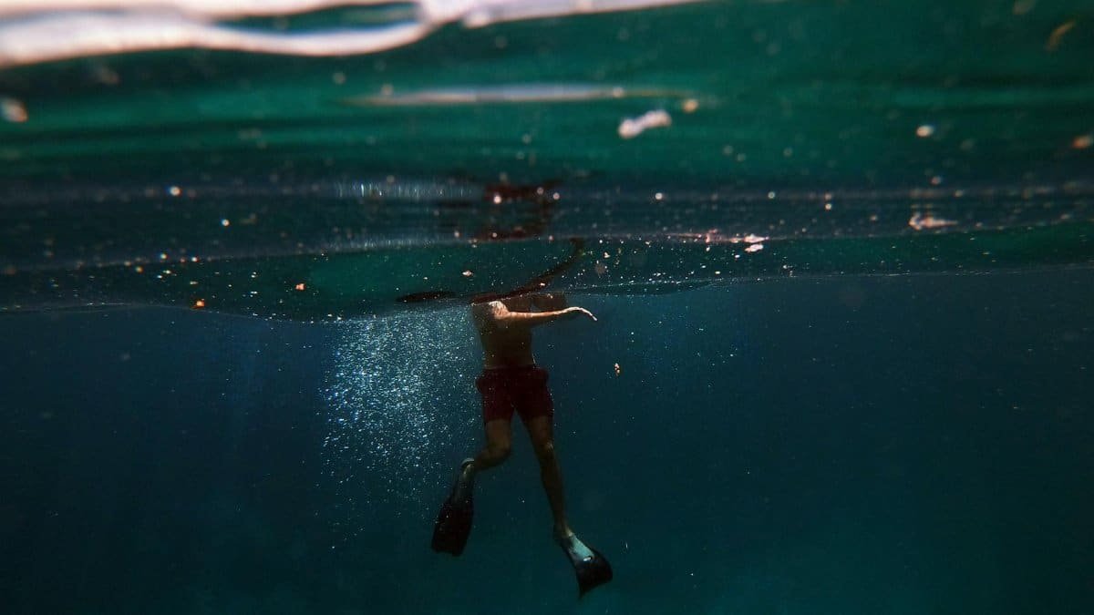 A person swimming underwater with fins in the clear Indonesian sea.