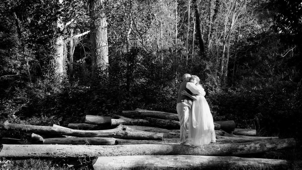 A tender moment between an elderly couple embracing in a sunlit forest clearing, depicting love and connection.