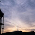 Silhouetted church tower with cross against a sunset sky in Plano, Texas.