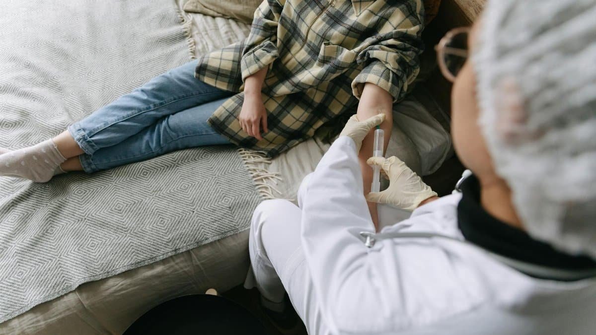 A healthcare professional carefully administers an injection to a patient sitting on a sofa in a cozy room.