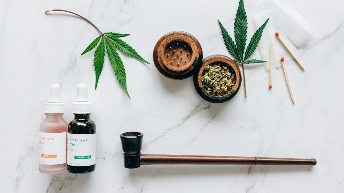 Top view of cannabis products including CBD oils, leaves, and smoking accessories on a marble surface.