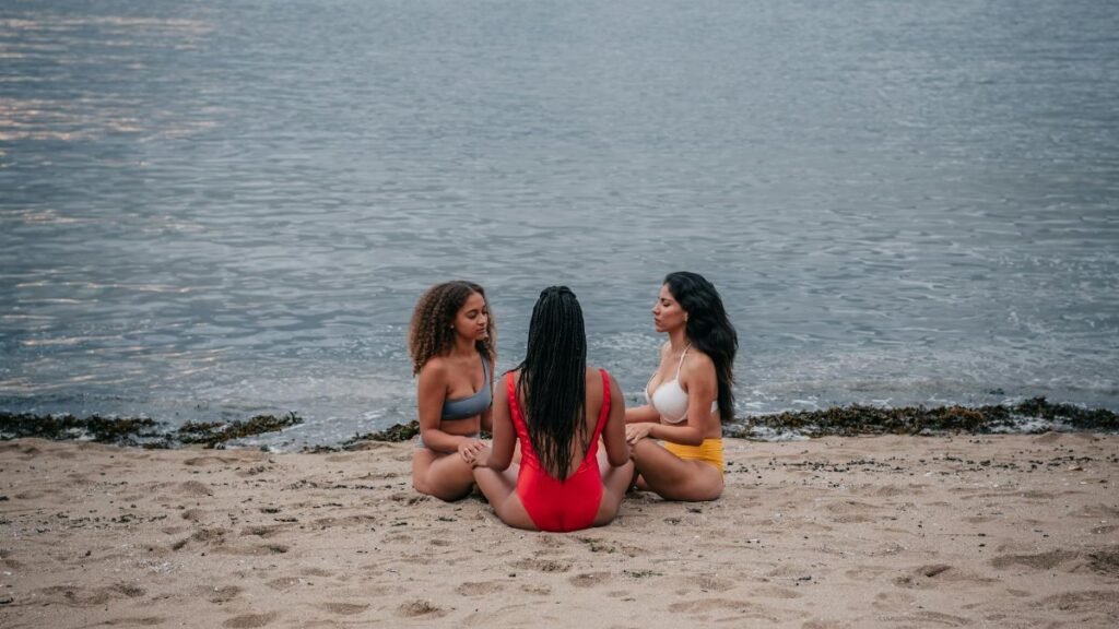 Three women meditating together on a serene seaside beach, embracing mindfulness and unity.