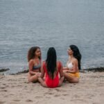 Three women meditating together on a serene seaside beach, embracing mindfulness and unity.
