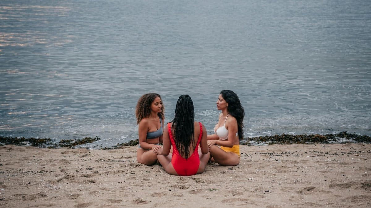 Three women meditating together on a serene seaside beach, embracing mindfulness and unity.