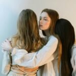 Three young women embracing each other in a serene indoor setting, evoking togetherness and empathy.