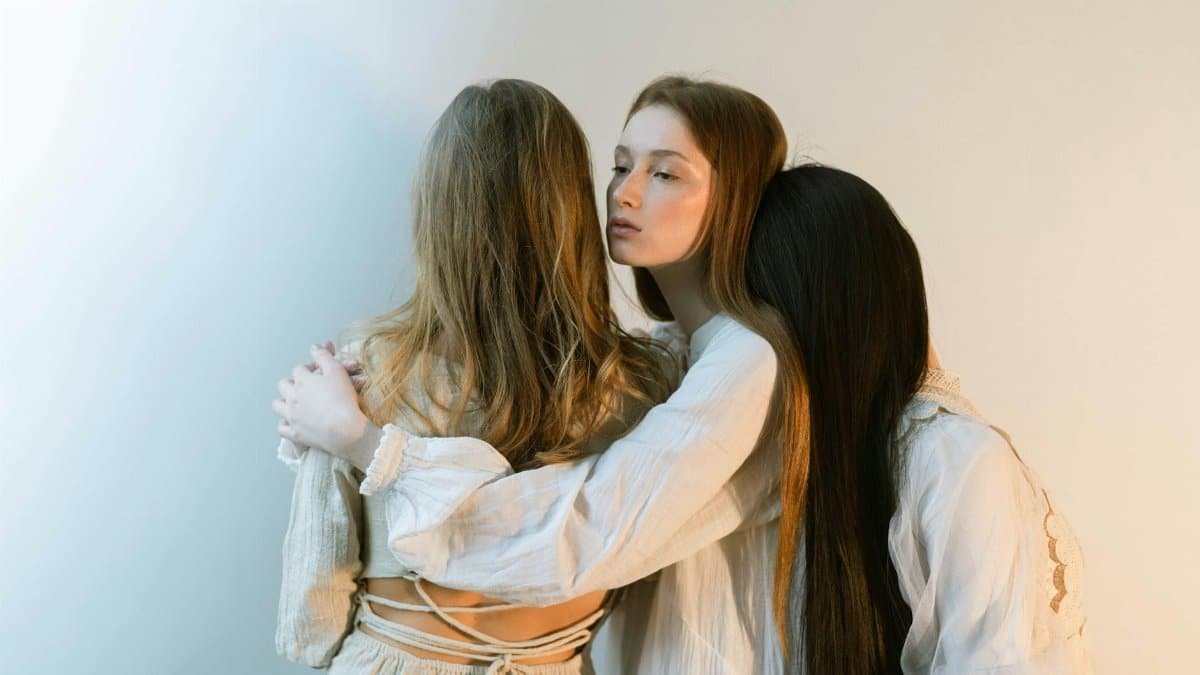 Three young women embracing each other in a serene indoor setting, evoking togetherness and empathy.