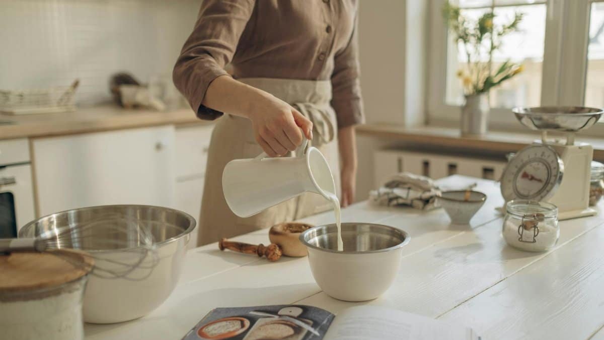 A person pours milk into a bowl, preparing ingredients on a kitchen island for baking.