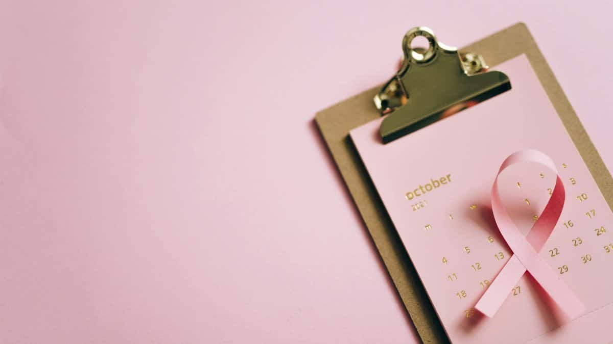 An overhead shot of an October calendar with a pink ribbon on a clipboard, symbolizing breast cancer awareness.