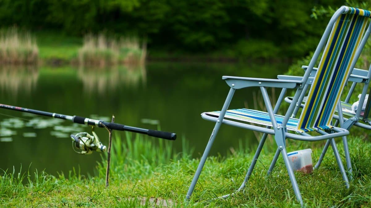 Relax by the lakeside with this inviting fishing setup and striped chairs for a perfect summer day.
