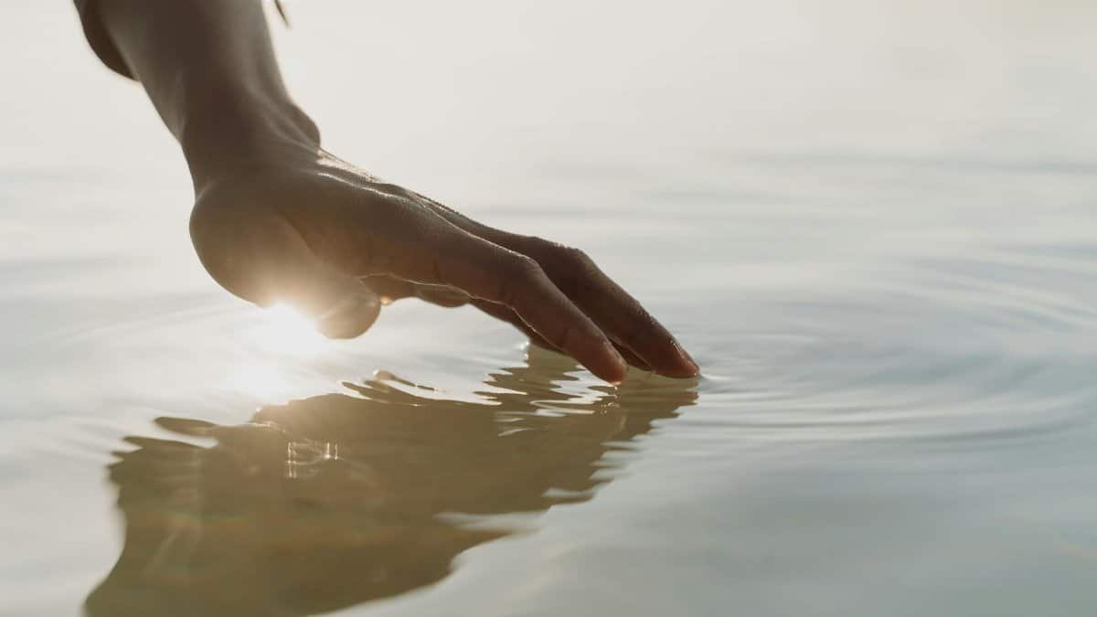 A tranquil scene of a hand gently touching the water, creating ripples with gentle sunlight reflection.